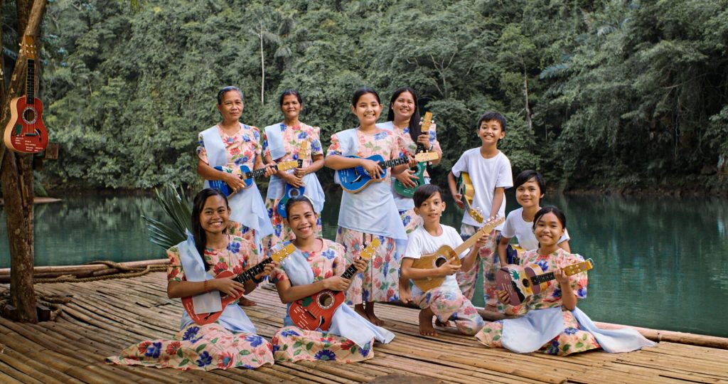 A group of women in colorful Filipiniana dresses joyfully holding rondalla instruments at at Loboc River Cruise